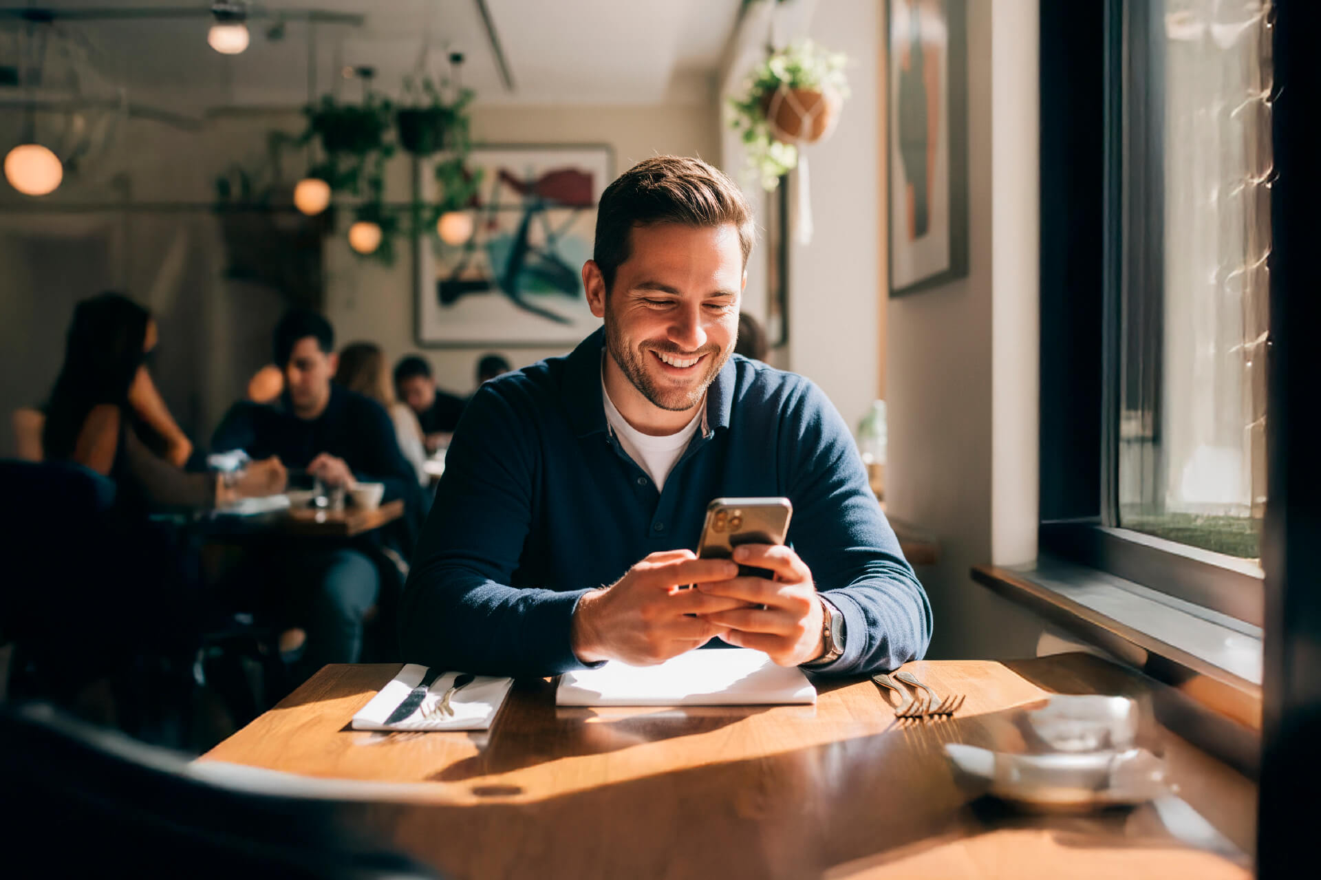 Persona sonriente usando su celular en un café, representando la facilidad de pedir préstamos digitales en línea desde cualquier lugar.